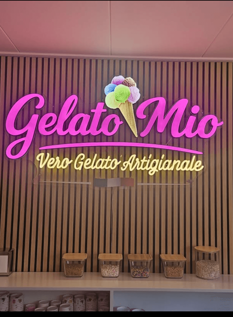 Het verlichte roze Gelato Mio-logo op de houten wand van de ijssalon in Soest